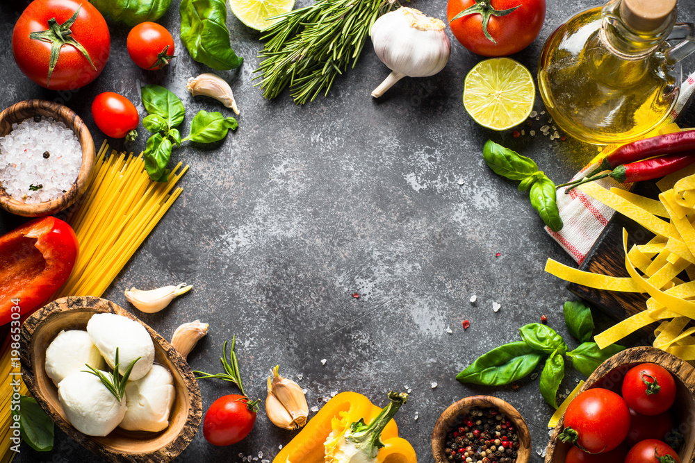 Pasta, tomatoes, cheese, basil and olive oil on black stone tabl