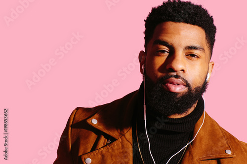 Fototapet Portrait of a cool man with beard and headphones isolated on pink studio backgro