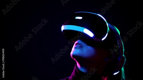 Young woman in VR headset looks around and wonders how amazing. Virtual reality helmet on black background