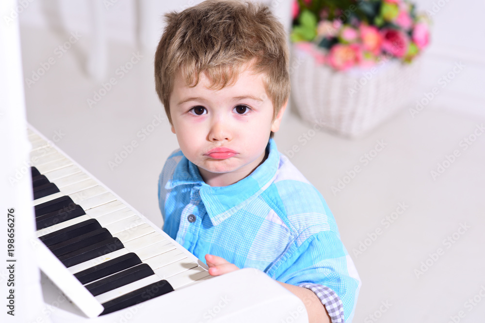 Child sit near piano keyboard, white background. Boy cute and adorable puts finger on keyboard of piano. Kid spend leisure near musical instrument. Elite childhood concept. Child sit near piano keyboard, white background. Boy cute and adorable puts finger on keyboard of piano. Kid spend leisure near musical instrument. Elite childhood concept.
