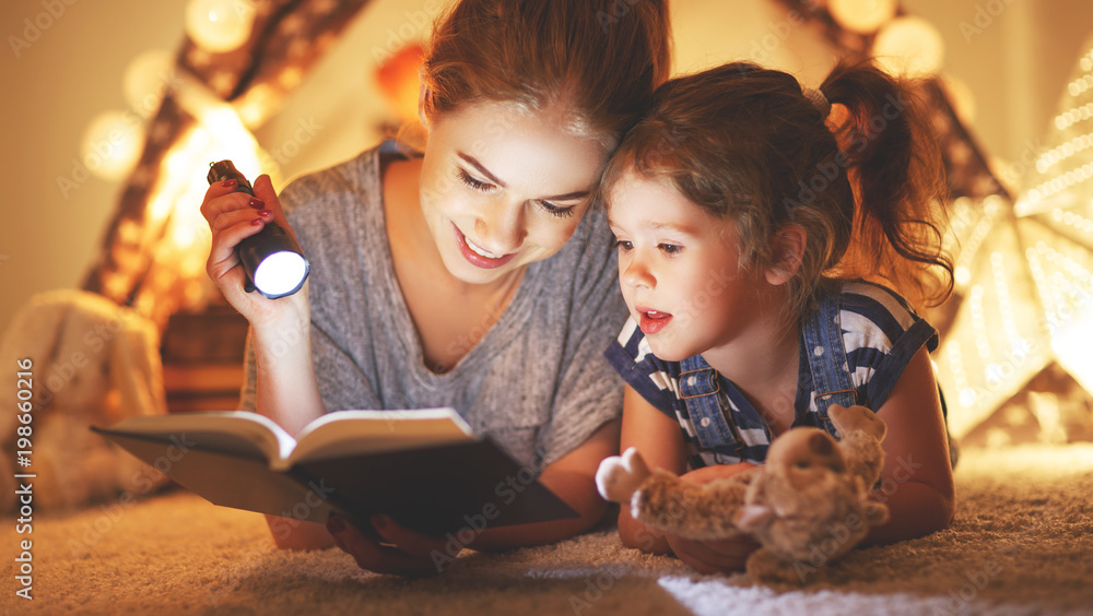 mother and child daughter reading a book and a flashlight before going to bed mother and child daughter reading a book and a flashlight before going to bed