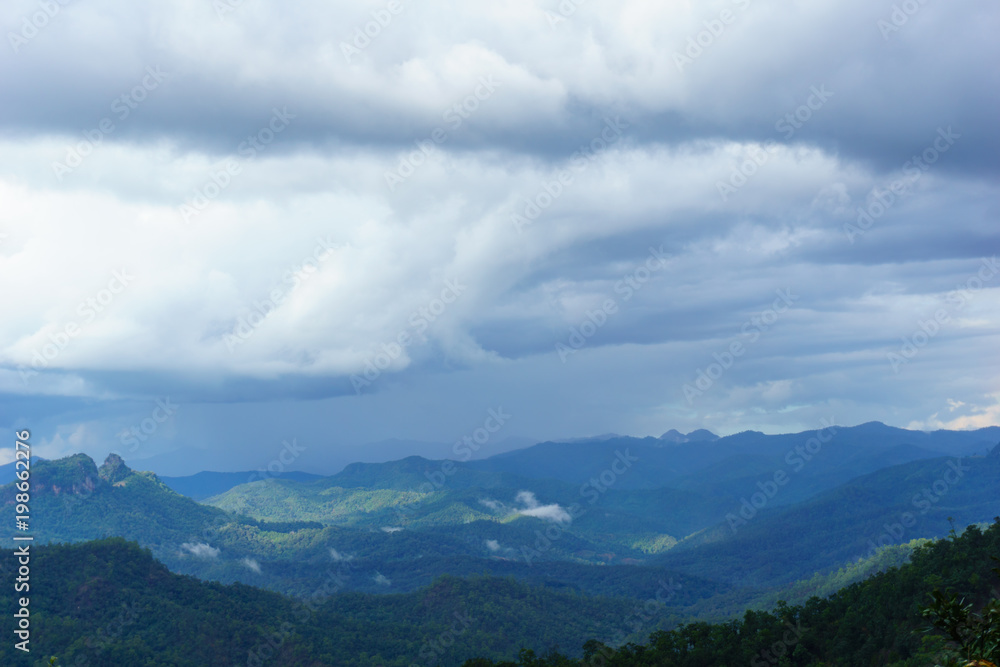 Amazing wild nature view of layer of mountain forest landscape with cloudy sky at winter season. Natural green scenery of cloud and mountain slopes background.