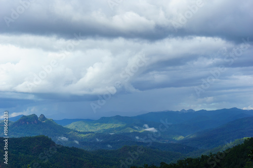 Amazing wild nature view of layer of mountain forest landscape with cloudy sky at winter season. Natural green scenery of cloud and mountain slopes background.