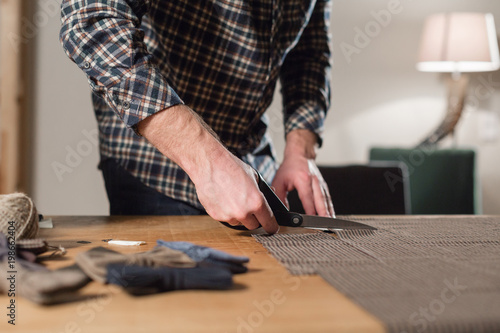 Closeup cutting brown plaid wool fabric. the line pattern. Young man working as a tailor and using a sewing machine in workshop.