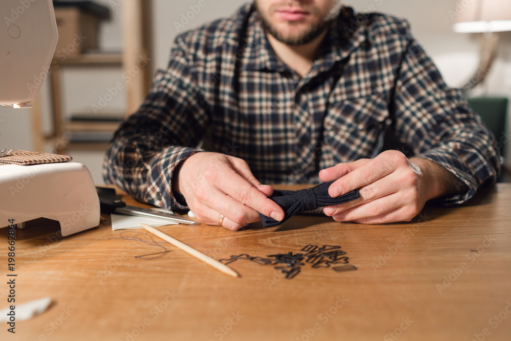 with a needle and thread in hand. Good looking young man working as a tailor and using a sewing machine in a textile studio. with a needle and thread in hand. Good looking young man working as a tailor and using a sewing machine in a textile studio.
