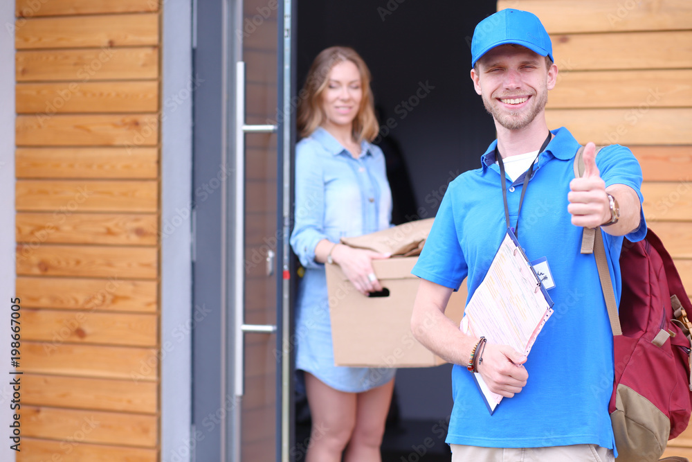 Smiling delivery man in blue uniform delivering parcel box to recipient - courier service concept Smiling delivery man in blue uniform delivering parcel box to recipient - courier service concept