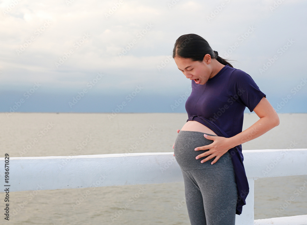 Excited pregnant woman touching her belly at seaside on the holiday.
