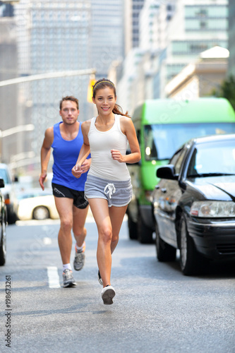 Happy couple runners exercising running outside on street. New York City active lifestyle, joggers athletes training outdoor in traffic.