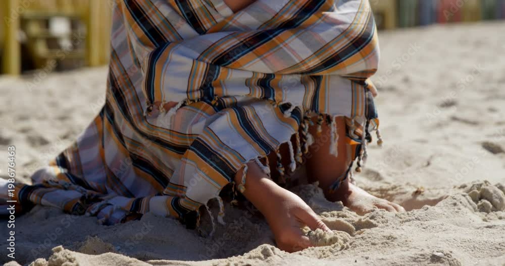 Teenage girl wrapped in blanket playing with sand Teenage girl wrapped in blanket playing with sand