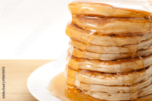 American pancake for breakfast, sweet snack and high calorie dessert concept with close up on flowing honey or maple syrup on a stack of thick pancakes isolated on white  background with copy space