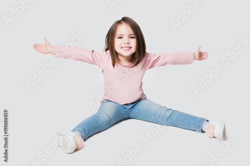 Funny little girl in jeans sitting on the floor looking at camera over white background 