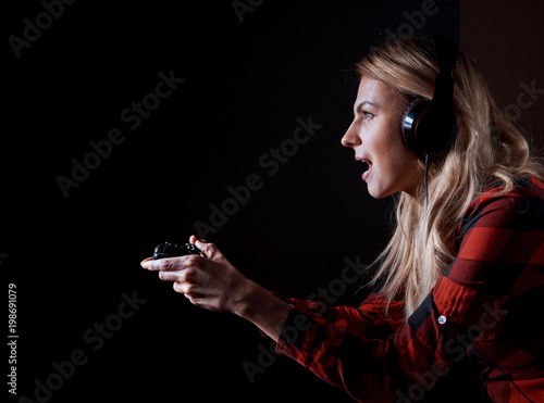 girl gamer in headphones and with a joystick enthusiastically playing on the console