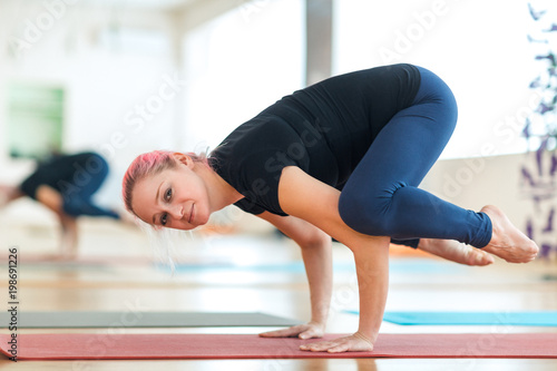 Sporty attractive woman with pink hair practicing yoga, standing in Crane exercise, Bakasana pose, working out in the gym