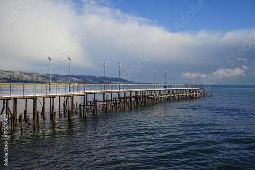 Seascape with old destroyed pier on the background of snow-capped hills. © vvicca