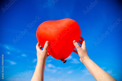     The girl holds the ball in the form of a heart against the blue sky 