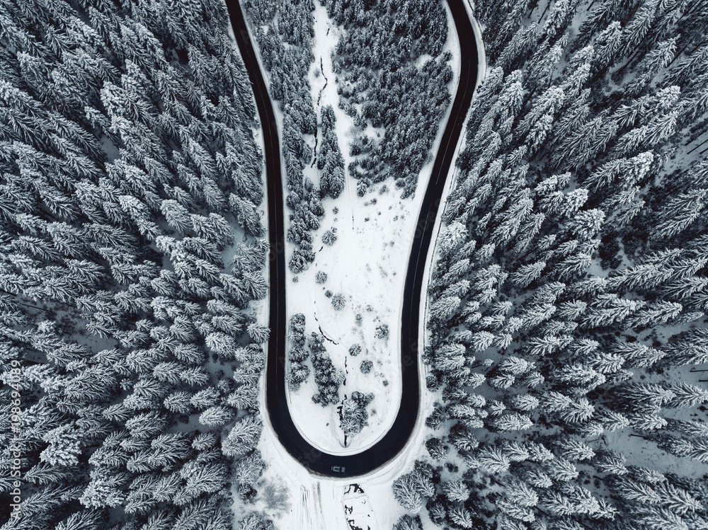 Aerial view of snowy forest with a curved road. Captured from above with a drone