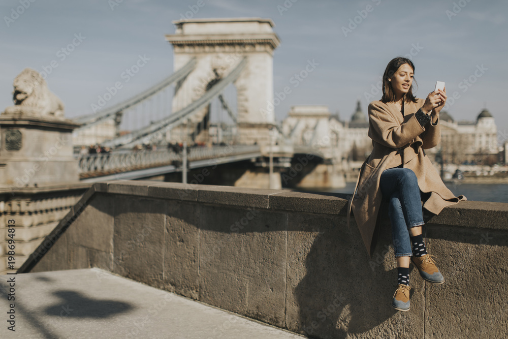Young woman using mobile phone with Chain bridge at background in Budapest Young woman using mobile phone with Chain bridge at background in Budapest