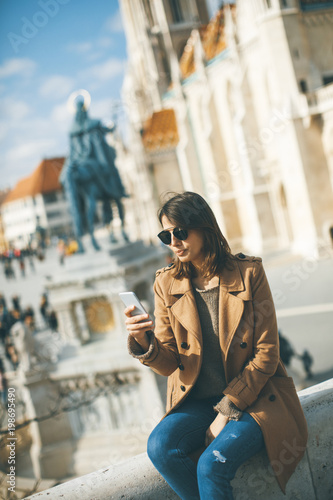 Trendy young woman sitting outdoor and using mobile phone