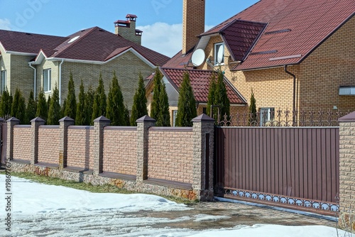 brown brick fence and iron closed gates on the street near the road in the snow