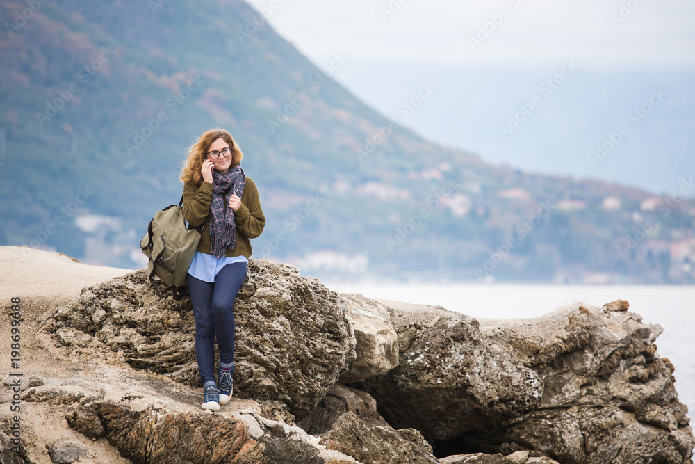 Woman traveler by the sea. On the horizon high mountains. Girl dressed in a sweater and scarf.