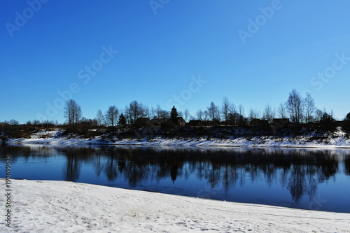 beautiful spring natural landscape sunny day, river among the snow-capped coasts against the blue sky, reflection of trees in the water, nature countryside