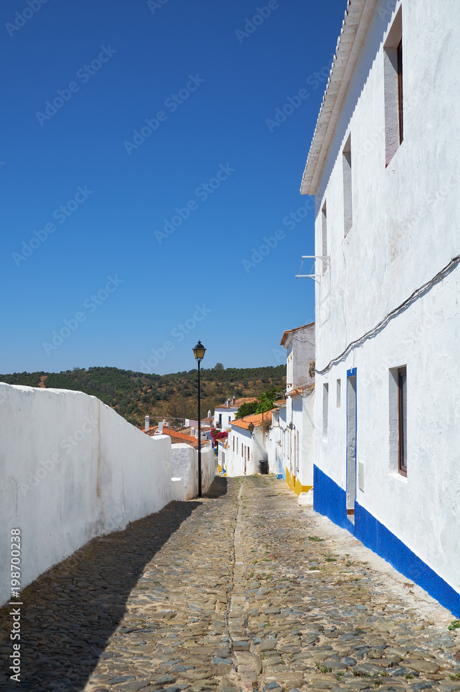 Cozy narrow paved streets with white houses inside the old city walls of Mertola. Beja. Portugal