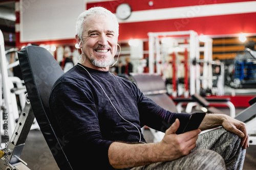 Adult happy man with gray hair listening to music with headphones in the gym photo