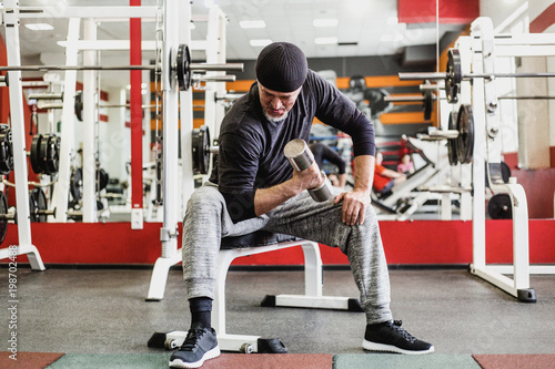 Adult athletic man doing exercise with dumbbells in gym