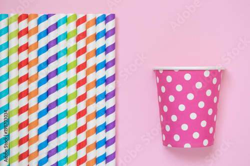 Multicolored drinking straws and paper party cup against rose background minimalistic concept