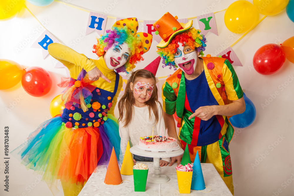 clown girl and clown boy at the children's birthday party. Festive table with a beautiful cake. Blow out candles and make a wish clown girl and clown boy at the children's birthday party. Festive table with a beautiful cake. Blow out candles and make a wish