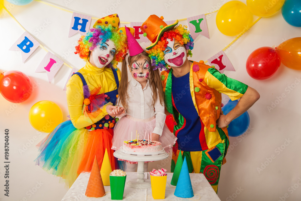 clown girl and clown boy at the children's birthday party. Festive table with a beautiful cake. Blow out candles and make a wish clown girl and clown boy at the children's birthday party. Festive table with a beautiful cake. Blow out candles and make a wish
