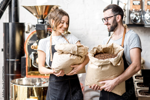 Fotografija Portrait of a two happy baristas in uniform standing with bags full of coffee be