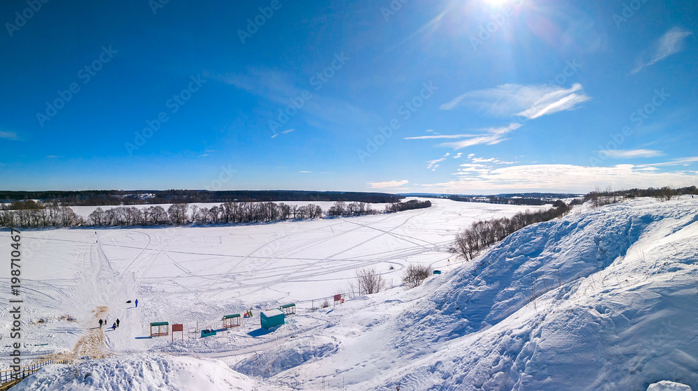 Beautiful ponamara in the winter. The river is covered with ice and snow. Winter landscape. Clear blue sky with clouds. Traces of people in the snow. Footpaths from shoes. Beautiful ponamara in the winter. The river is covered with ice and snow. Winter landscape. Clear blue sky with clouds. Traces of people in the snow. Footpaths from shoes.