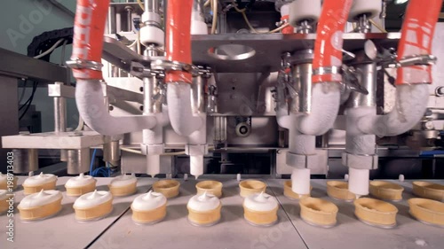 Four industrial pipes are filling moving wafer cups with ice-cream substance 