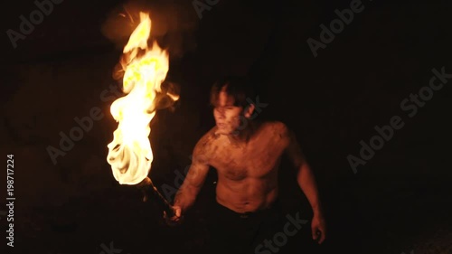 Careful hermit with burning torch in hand walks and looks around in stone cave photo