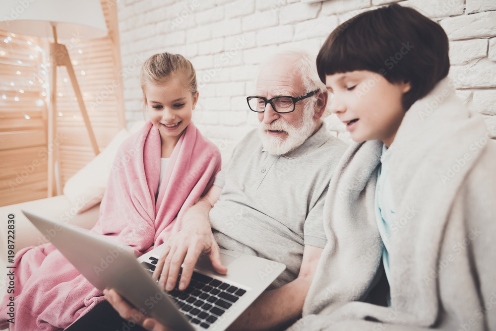 Obraz premium Grandfather, grandson and granddaughter at home. Grandpa and children are watching movie on laptop.
