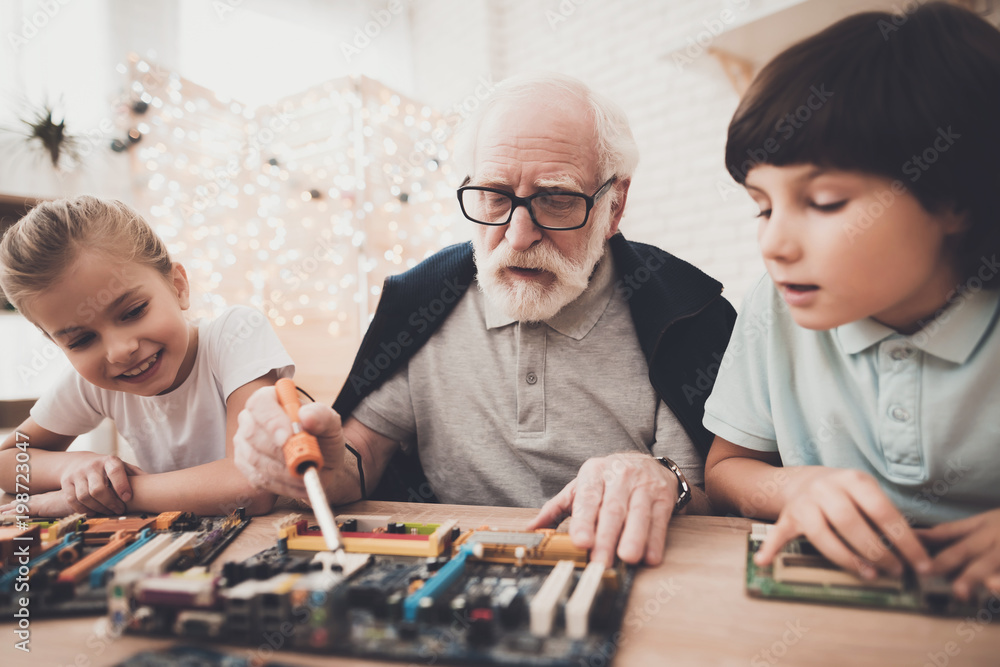 Fototapeta premium Grandfather, grandson and granddaughter at home. Grandpa teaches children how to braze.