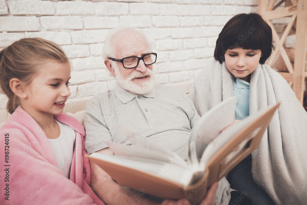 Grandfather, grandson and granddaughter at home. Grandpa and children are watching photos in album. Grandfather, grandson and granddaughter at home. Grandpa and children are watching photos in album.