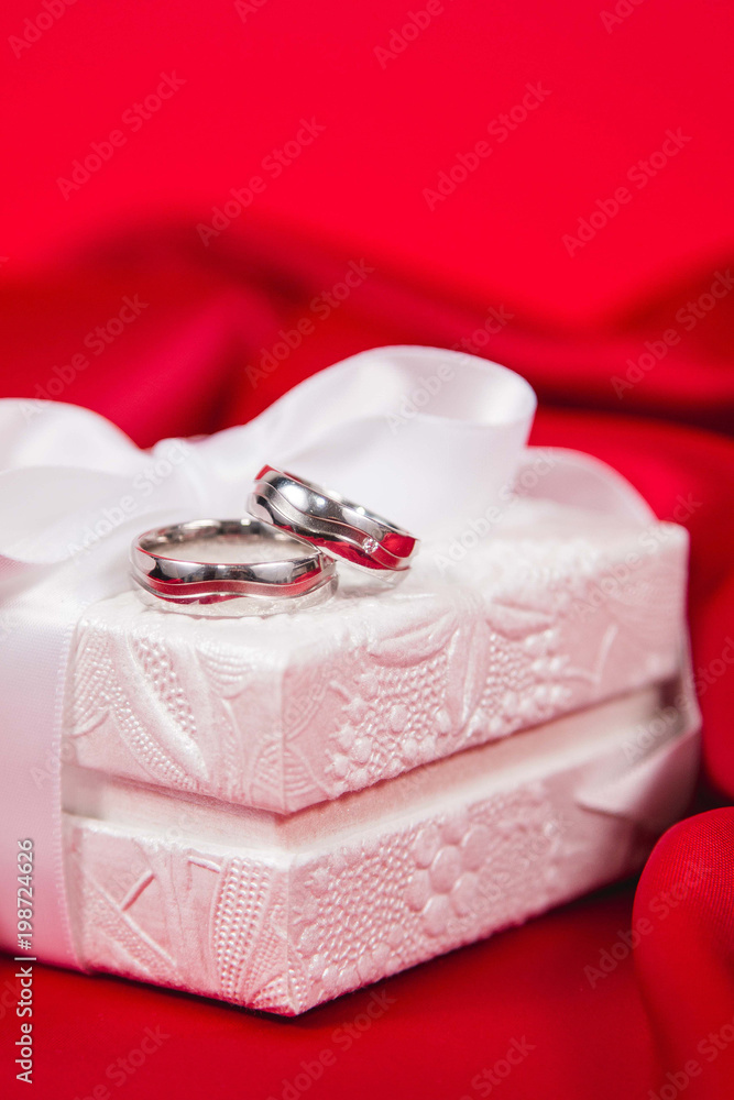 Beautiful close up of wedding rings on white luxury box on red silk background