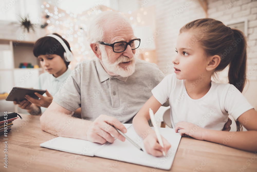 Grandfather, grandson and granddaughter at home. Grandpa is helping girl with homework. Grandfather, grandson and granddaughter at home. Grandpa is helping girl with homework.