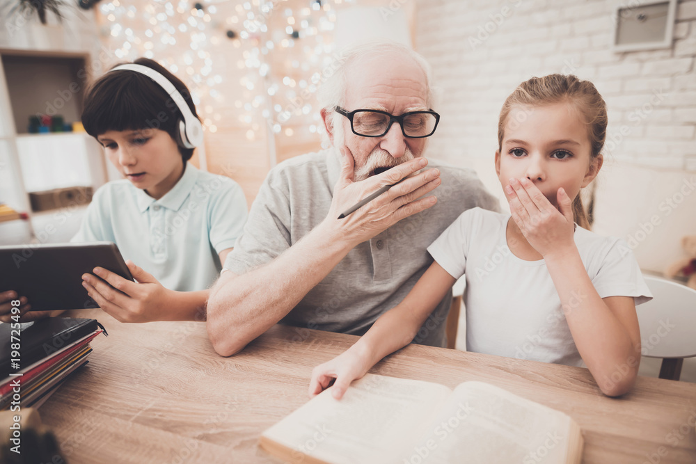 Grandfather, grandson and granddaughter at home. Grandpa is helping girl with homework. Grandfather, grandson and granddaughter at home. Grandpa is helping girl with homework.