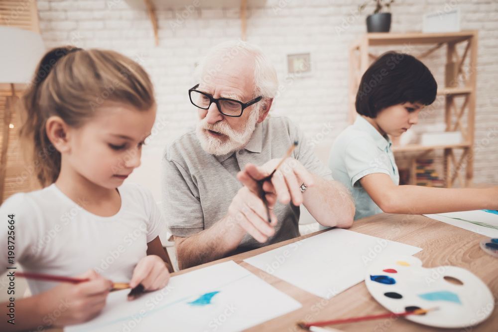 Grandfather, grandson and granddaughter at home. Grandpa is helping children paint. Grandfather, grandson and granddaughter at home. Grandpa is helping children paint.