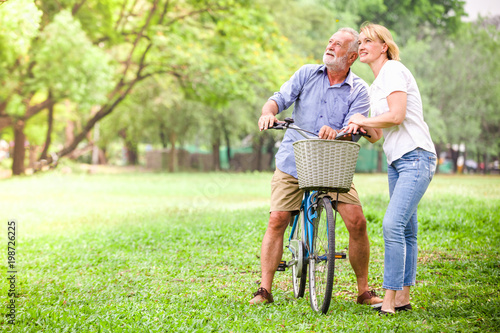 Senior couple walking their bike along happily talking happily.