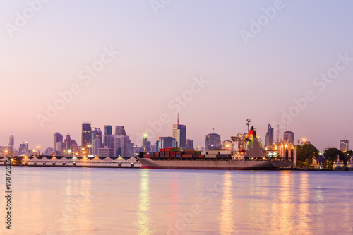 Shipping working loading containers by crane in ship on the night,Cityscape background