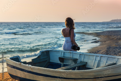 Beautiful naked  female photographer in the pareo with professional camera near boat on the sand © flowertiare