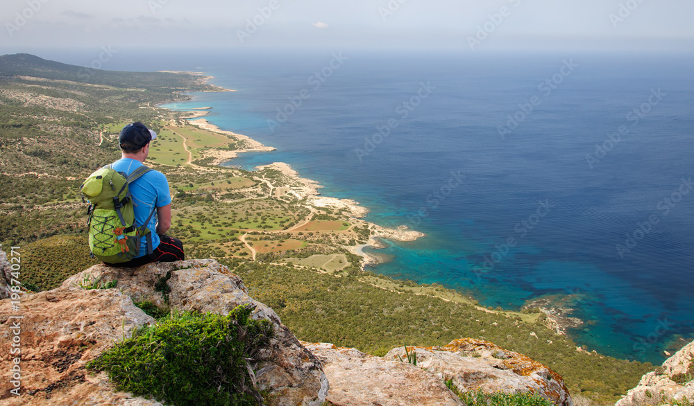 man with backpack sitting on a rock and looking at the Mediterranean Sea