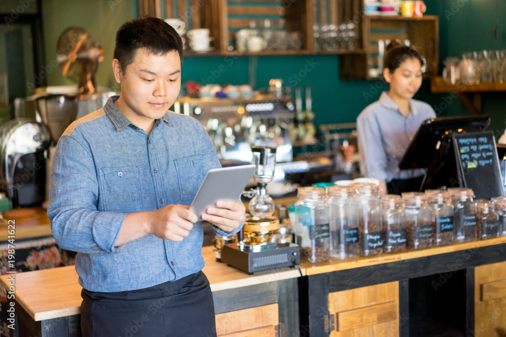 Content handsome young cafe employee using tablet as personal organizer