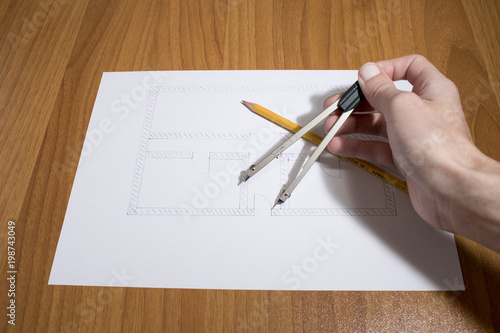 Person drawing a house project with compass and pencil on a table photo