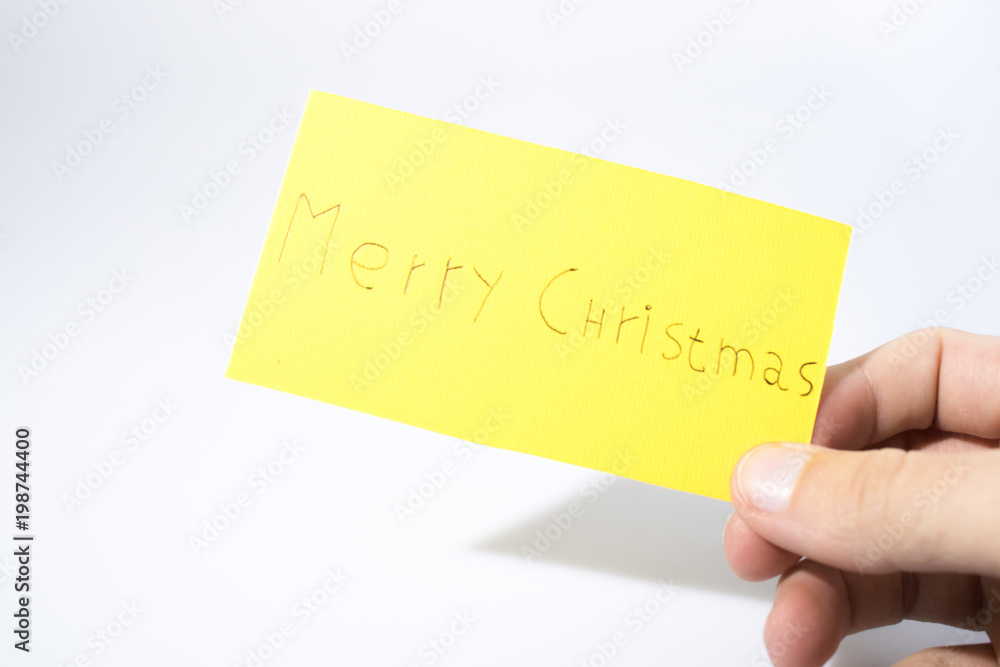 Merry christmas handwrite with a hand on a yellow paper Merry christmas handwrite with a hand on a yellow paper