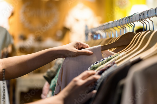 Close up of woman hand choosing thrift young and discount t-shirt clothes in store, searching or buying cheap cotton shirt on rack hanger at flea market , stall shopping apparel fashion concept